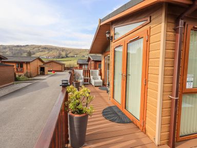 A balcony with potted plants and chairs overlooking wooden cabins and hills at Valley View Lodge Wansfell 10 Limefitt Park near Windermere