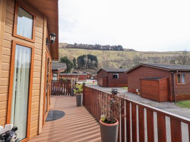 A wooden deck with potted plants outside wooden cabins with hills in the background at Valley View Lodge Wansfell 10 Limefitt Park near Windermere