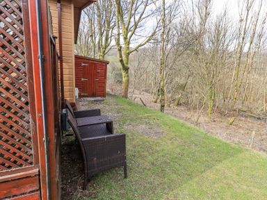 An outdoor area with two chairs next to a wooden building a small wooden shed and trees in the background at Valley View Lodge Wansfell 10 Limefitt Park near Windermere
