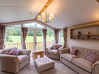 A living room with beige sofas a wooden coffee table and large windows with curtains at Latterbarrow Lodge in Beckside 46 Limefitt Park near Windermere