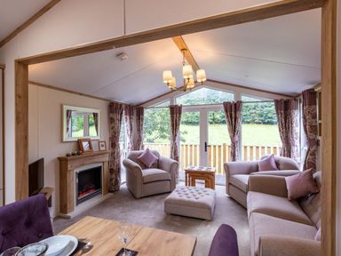 A living room with armchairs a sofa an ottoman fireplace and large windows at Latterbarrow Lodge Beckside 46 Limefitt Park near Windermere
