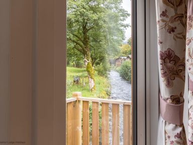 A view of a river and trees from a window with floral curtains at Latterbarrow Lodge Beckside 46 Limefitt Park near Windermere