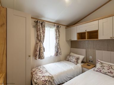 A bedroom with two single beds with floral bedding and a window with floral curtains at Latterbarrow Lodge Beckside 46 Limefitt Park near Windermere
