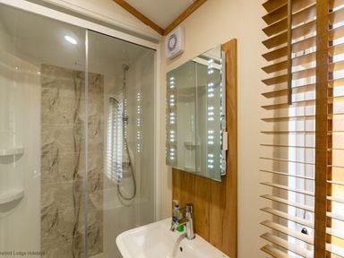 A bathroom with a sink a mirror with lights a shower area and wooden blinds at Latterbarrow Lodge Beckside 46 Limefitt Park near Windermere