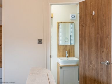 A bathroom with a sink and mirror next to a wooden door at Latterbarrow Lodge Beckside 46 Limefitt Park near Windermere