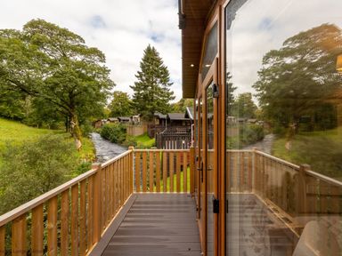 A wooden balcony overlooking a narrow river and trees at Latterbarrow Lodge in Beckside 46 Limefitt Park near Windermere
