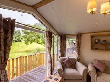 A sitting area with armchairs and a wooden balcony overlooking a green field at Latterbarrow Lodge Beckside 46 Limefitt Park near Windermere