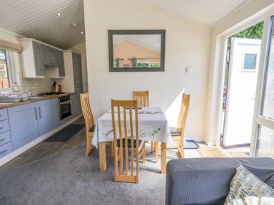 A dining area with wooden chairs and a table beside a kitchen and glass door at Robin View Lodge Beckside 3 Limefitt Park near Windermere