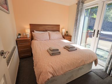 A bedroom with a double bed pink bedding towels on bed bedside tables with lamps and plants and glass doors leading outside at Robin View Lodge Beckside 3 Limefitt Park near Windermere