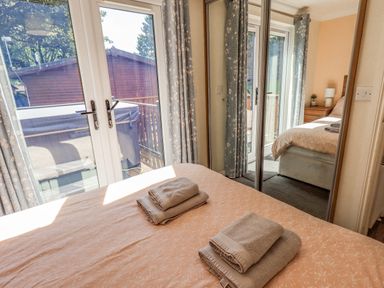 A bedroom with a bed, folded towels on the bed, glass doors leading outside, curtains, and mirrored wardrobe doors at Robin View Lodge Beckside 3 Limefitt Park near Windermere