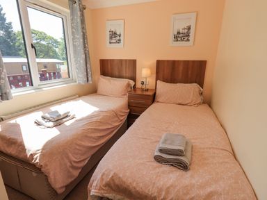 A bedroom with two single beds with peach bedding a bedside table with a lamp and folded towels on each bed at Robin View Lodge Beckside 3 Limefitt Park near Windermere