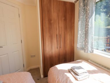A bedroom with two single beds a wooden wardrobe a window with floral curtains and towels on a bed at Robin View Lodge Beckside 3 Limefitt Park near Windermere