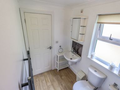 A bathroom with a white door a wall-mounted sink a mirror cabinet a toilet a window and a small white storage shelf at Robin View Lodge Beckside 3 Limefitt Park near Windermere