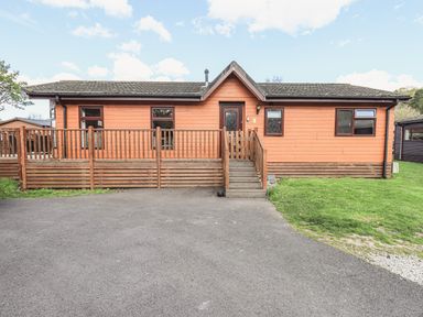 An exterior view of a single-story wooden lodge with a small porch and steps leading to the front door at Sunny Brow Lodge Lakeside 5 White Cross Bay near Windermere