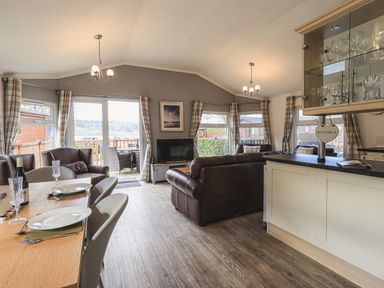 A living room with dining table set with plates and glasses and leather sofas at Sunny Brow Lodge Lakeside 5 White Cross Bay near Windermere