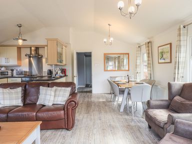 A living room with a brown leather sofa and armchair and a dining table set with six chairs at Sunny Brow Lodge Lakeside 5 White Cross Bay near Windermere