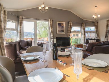 A dining table set with plates and glasses in a living room with sofas and a television at Sunny Brow Lodge Lakeside 5 White Cross Bay near Windermere