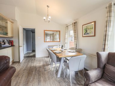 A dining area with a wooden table set for six people surrounded by modern chairs and a large mirror on the wall at Sunny Brow Lodge Lakeside 5 White Cross Bay near Windermere