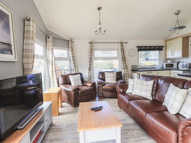 A living room with brown leather sofas a wooden coffee table a television and large windows at Sunny Brow Lodge Lakeside 5 White Cross Bay near Windermere