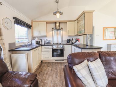 A kitchen with white cabinets black countertops and brown leather sofas at Sunny Brow Lodge Lakeside 5 White Cross Bay near Windermere