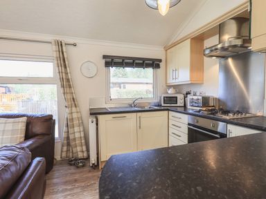 A kitchen with white cabinets black countertops a window microwave toaster and gas stove at Sunny Brow Lodge Lakeside 5 White Cross Bay near Windermere