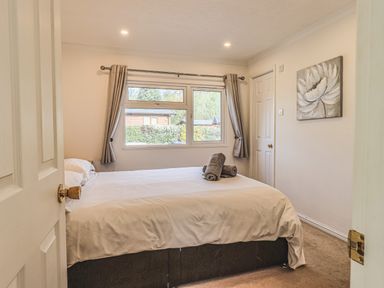 A bedroom with a bed and towels on it by a window with curtains and a flower painting on the wall at Sunny Brow Lodge Lakeside 5 White Cross Bay near Windermere