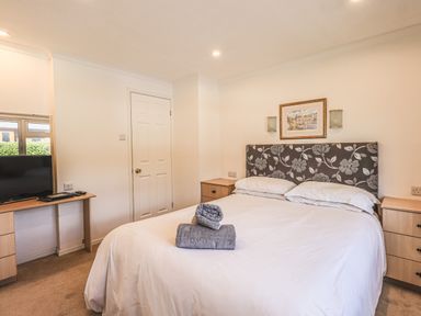 A bedroom with a bed with floral headboard and towels on it a television on a desk and two wooden cabinets on each side of the bed at Sunny Brow Lodge in Lakeside 5 White Cross Bay near Windermere