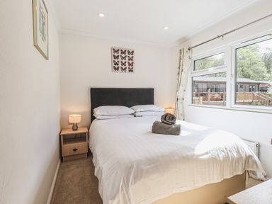 A bedroom with a double bed bedside tables lamps and a window showing cabins outside at Sunny Brow Lodge Lakeside 5 White Cross Bay near Windermere
