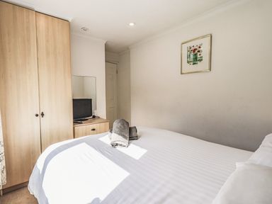 A bedroom with a double bed towels on the bed wardrobe and a small TV on a dresser at Sunny Brow Lodge Lakeside 5 White Cross Bay near Windermere