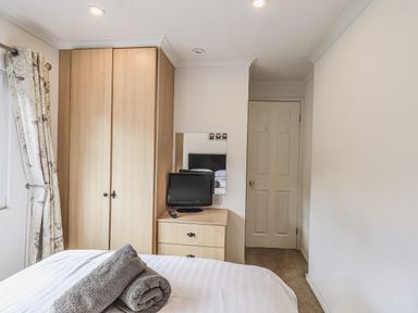 A bedroom with a bed and rolled towels a wardrobe a dresser with a small television and a mirror at Sunny Brow Lodge Lakeside 5 White Cross Bay near Windermere