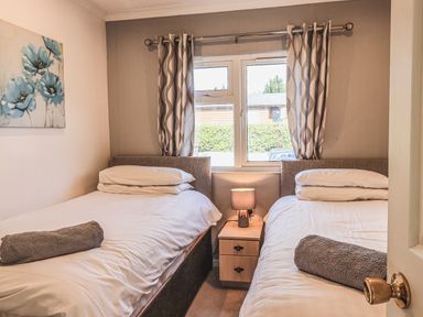 A bedroom with two single beds separated by a nightstand and lamp with a window and curtains at Sunny Brow Lodge Lakeside 5 White Cross Bay near Windermere