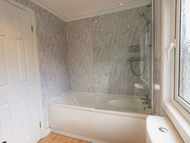 A bathroom with a bathtub shower combination a glass shower screen and a window at Sunny Brow Lodge Lakeside 5 White Cross Bay near Windermere