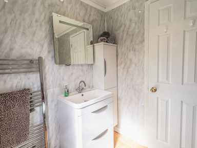 A bathroom with a white sink cabinet mirror a white storage cabinet and a towel on a heated rack at Sunny Brow Lodge Lakeside 5 White Cross Bay near Windermere