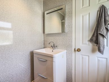 A bathroom with a white sink cabinet a mirror above it a closed white door and a gray towel hanging on the door at Sunny Brow Lodge Lakeside 5 White Cross Bay near Windermere