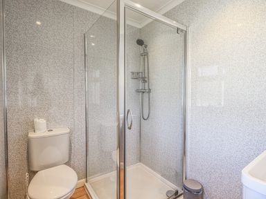 A bathroom with a toilet a glass shower enclosure with a showerhead and a small trash bin at Sunny Brow Lodge Lakeside 5 White Cross Bay near Windermere