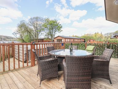 An outdoor deck with a round glass table and six wicker chairs at Sunny Brow Lodge in Lakeside 5 White Cross Bay near Windermere