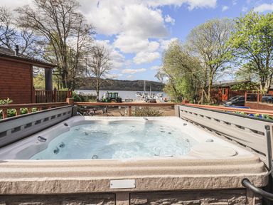 An outdoor hot tub on a deck with trees boats and a lake in the background at Sunny Brow Lodge Lakeside 5 White Cross Bay near Windermere
