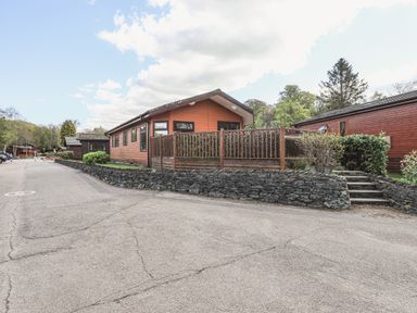 A wooden lodge with a fenced porch and stone steps leading up from a paved road at Sunny Brow Lodge Lakeside 5 White Cross Bay near Windermere