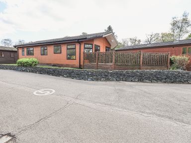 A wooden lodge with multiple windows and a fenced garden area by a paved road marked with a 5 speed limit at Sunny Brow Lodge in Lakeside 5 White Cross Bay near Windermere