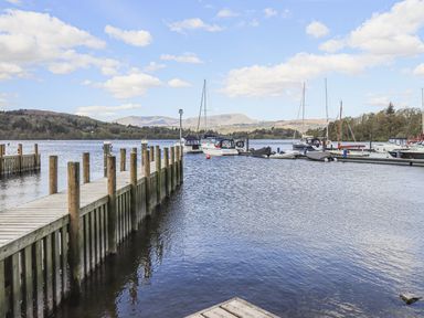 A wooden dock extending into a lake with boats moored at the side and hills in the background at Sunny Brow Lodge Lakeside 5 White Cross Bay near Windermere