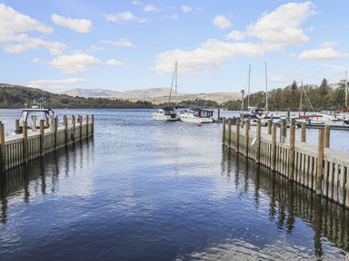 A lake with boats docked alongside wooden piers and hills in the background at Sunny Brow Lodge Lakeside 5 White Cross Bay near Windermere
