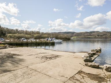 A boat dock with several boats moored next to a concrete boat ramp and a lake surrounded by hills at Badgers Hollow Lodge Grasmere 30 White Cross Bay near Windermere