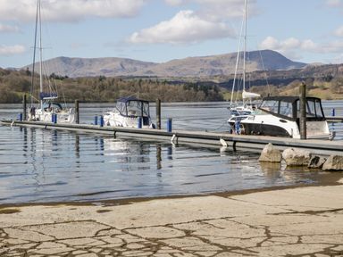 A dock with several boats moored on a lake with hills in the background at Badgers Hollow Lodge Grasmere 30 White Cross Bay near Windermere
