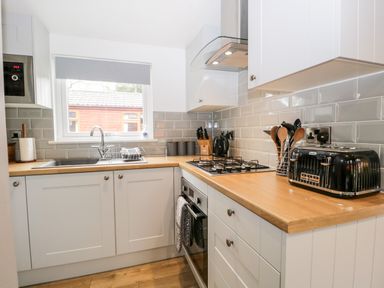 A kitchen with white cabinets wooden countertops a gas stove a black toaster and a window at Badgers Hollow Lodge Grasmere 30 White Cross Bay near Windermere