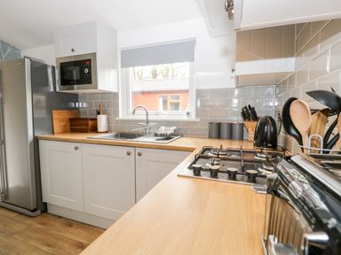 A kitchen with a stainless steel refrigerator a microwave a double sink a gas stove wooden utensils and grey storage containers at Badgers Hollow Lodge in Grasmere 30 White Cross Bay near Windermere