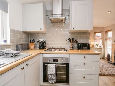 A kitchen with white cabinets a gas stove a kettle a toaster and kitchen utensils at Badgers Hollow Lodge Grasmere 30 White Cross Bay near Windermere