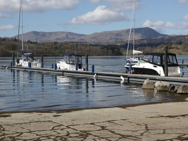 A dock with several boats moored on a lake with mountains in the background at Pinehaven Lodge Grasmere 6 White Cross Bay near Windermere