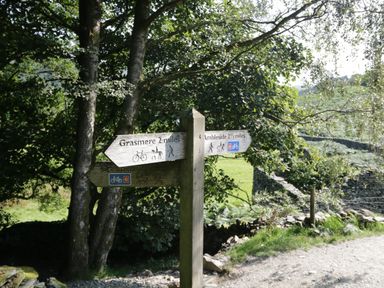 A wooden signpost with directions to Grasmere and Ambleside in a rural outdoor setting at Pinehaven Lodge in Grasmere 6 White Cross Bay near Windermere