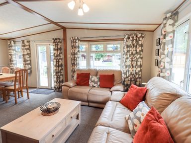 A living room with leather sofas and a wooden coffee table near windows with floral curtains at Pinehaven Lodge Grasmere 6 White Cross Bay near Windermere