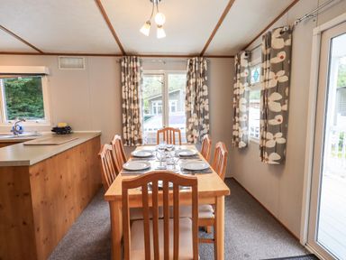 A dining area with a wooden table set for six and floral curtains at Pinehaven Lodge Grasmere 6 White Cross Bay near Windermere
